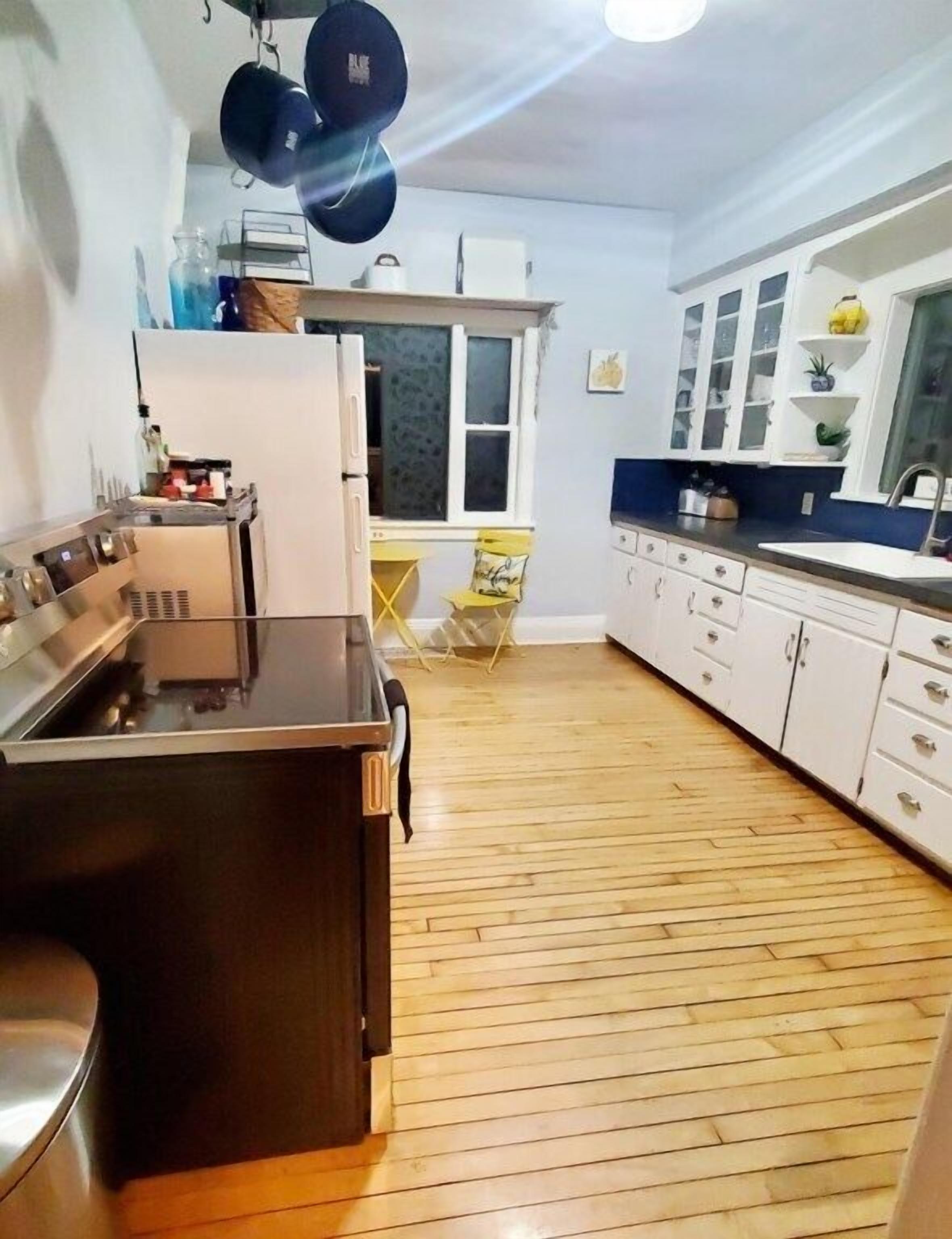 A modern kitchen with a central island, white cabinets, and a wooden floor.