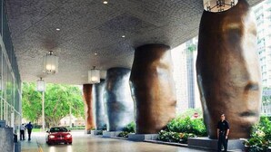 Un bâtiment moderne doté de grandes colonnes cylindriques, avec une voiture rouge garée devant.