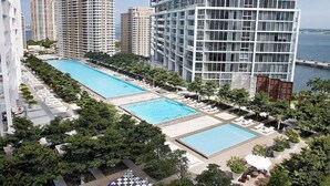 Un immeuble de grande hauteur doté de deux piscines, entouré de verdure et offrant une vue sur la mer.