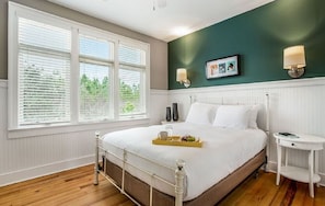 A bedroom with a bed, bedside tables, a window with blinds, and a green accent wall. - The Cabins at Gulf State Park (Gulf Shores)