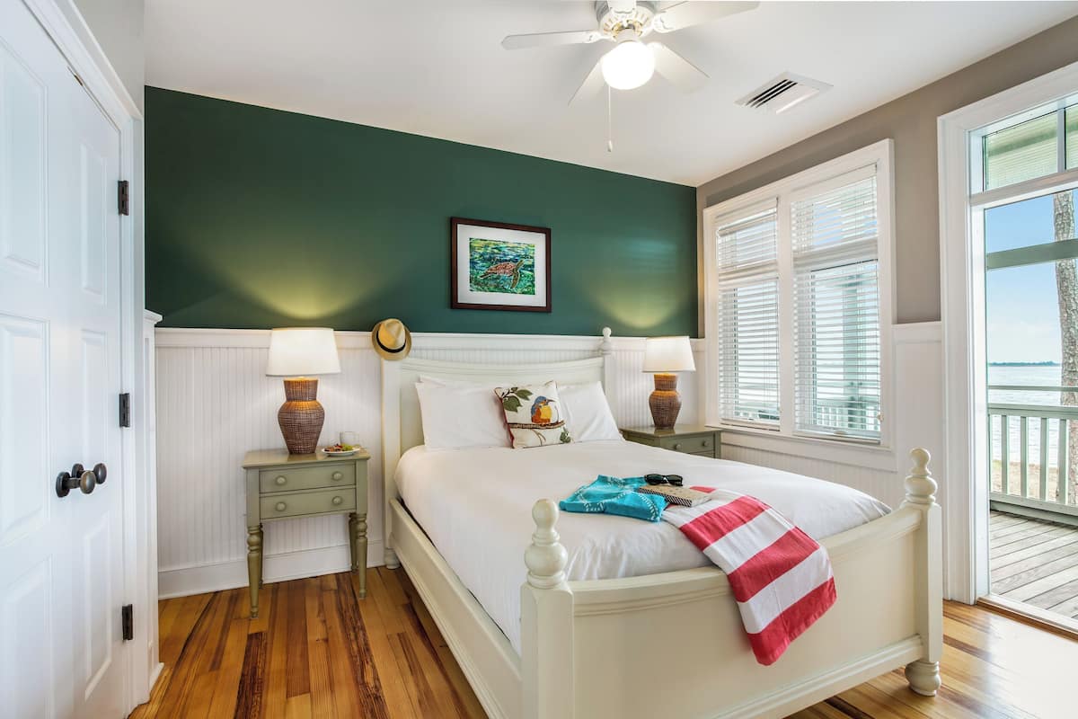 A bedroom with a white bed, two nightstands, a ceiling fan, and a view of the outdoors.