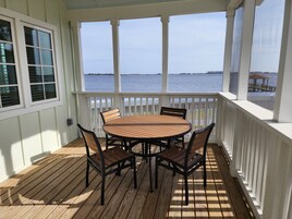 A covered outdoor area with a wooden deck, a round table with chairs, and a view of the water.