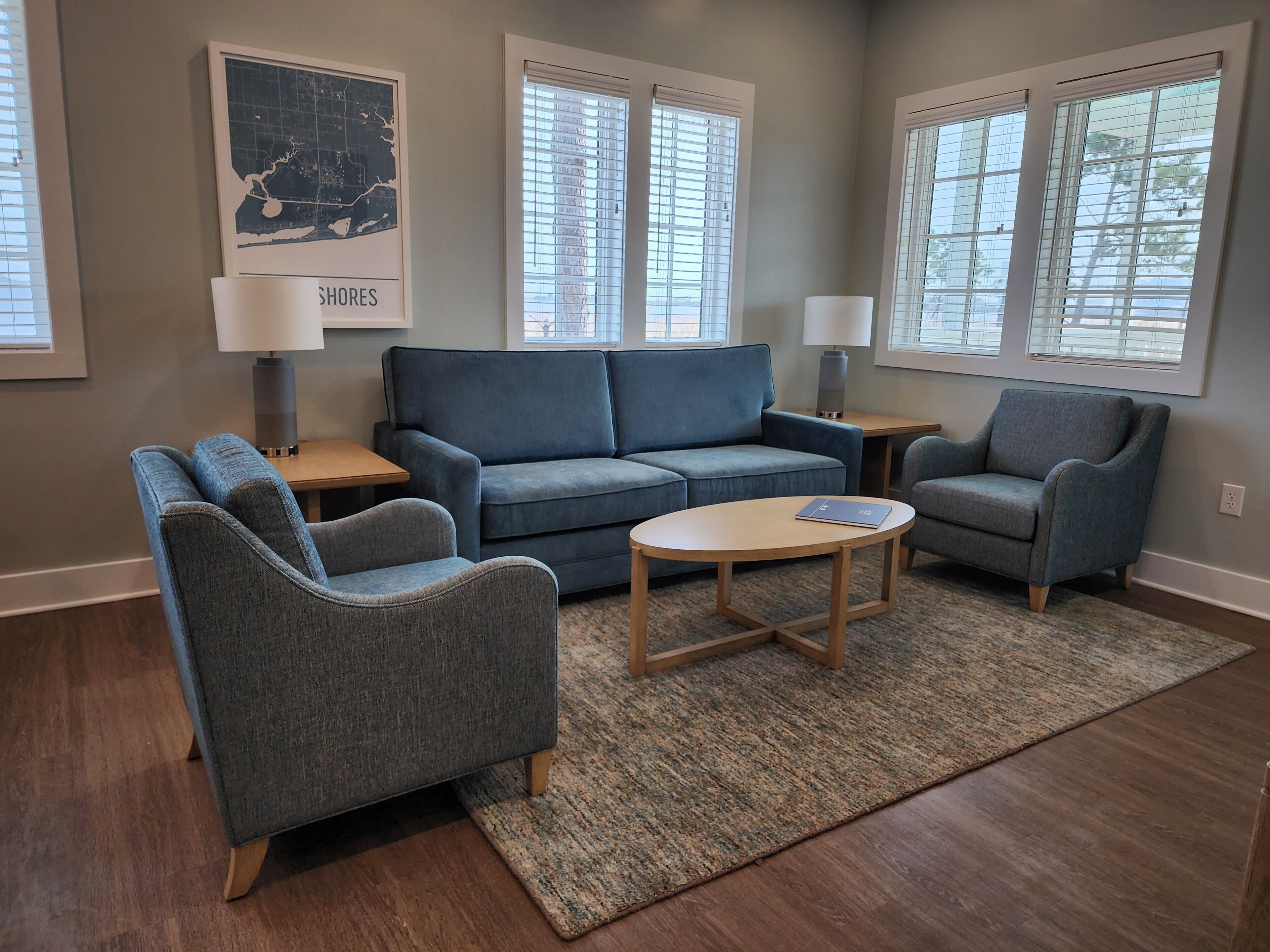 A living room with a blue sofa, two armchairs, a coffee table, and a rug. There are two lamps on side tables and a map on the wall.