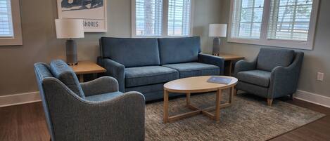 A living room with a blue sofa, two armchairs, a coffee table, and a rug. There are two lamps on side tables and a map on the wall.