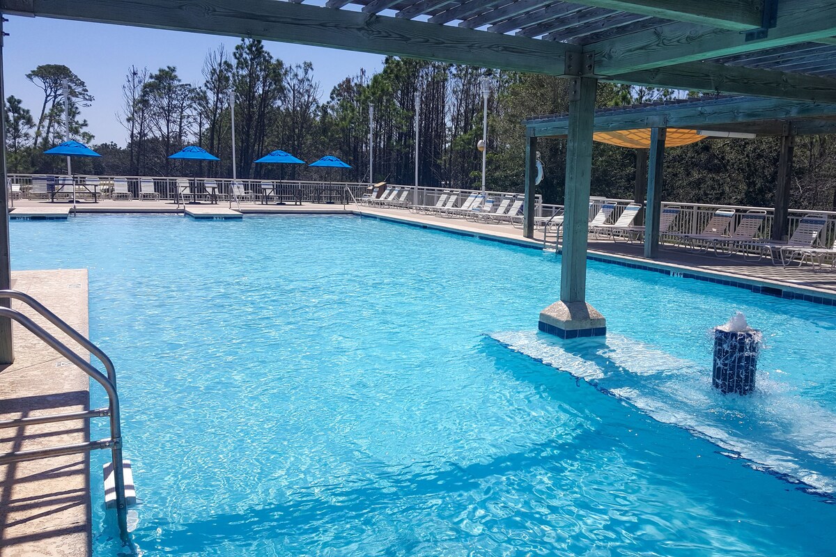 Una piscina con una fuente de agua, sillas de descanso y sombrillas.