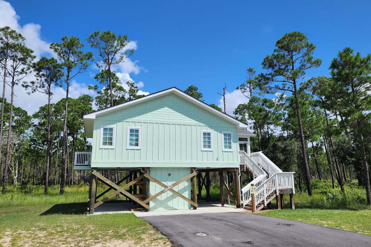 A light blue house with a covered porch and a staircase leading to a deck.