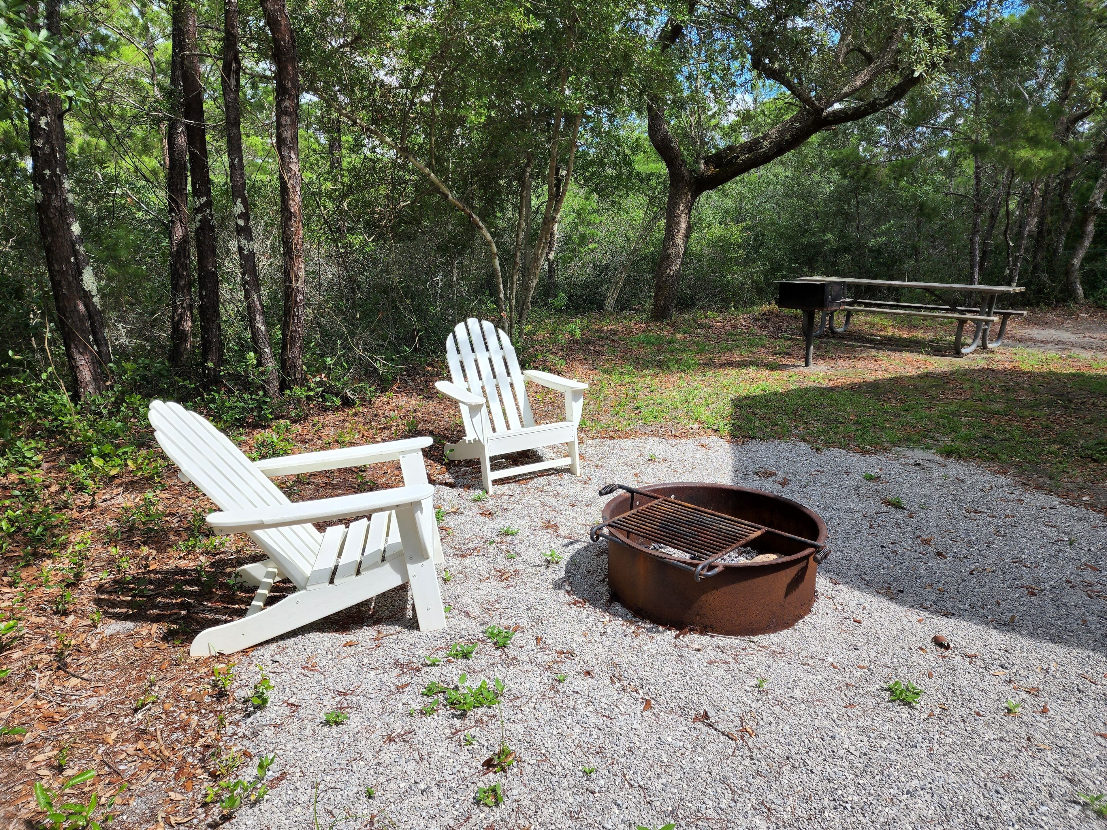 En campingplads med to Adirondack-stole, en grill i metal og et picnicbord.