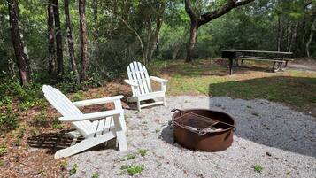 En campingplads med to Adirondack-stole, en grill i metal og et picnicbord.