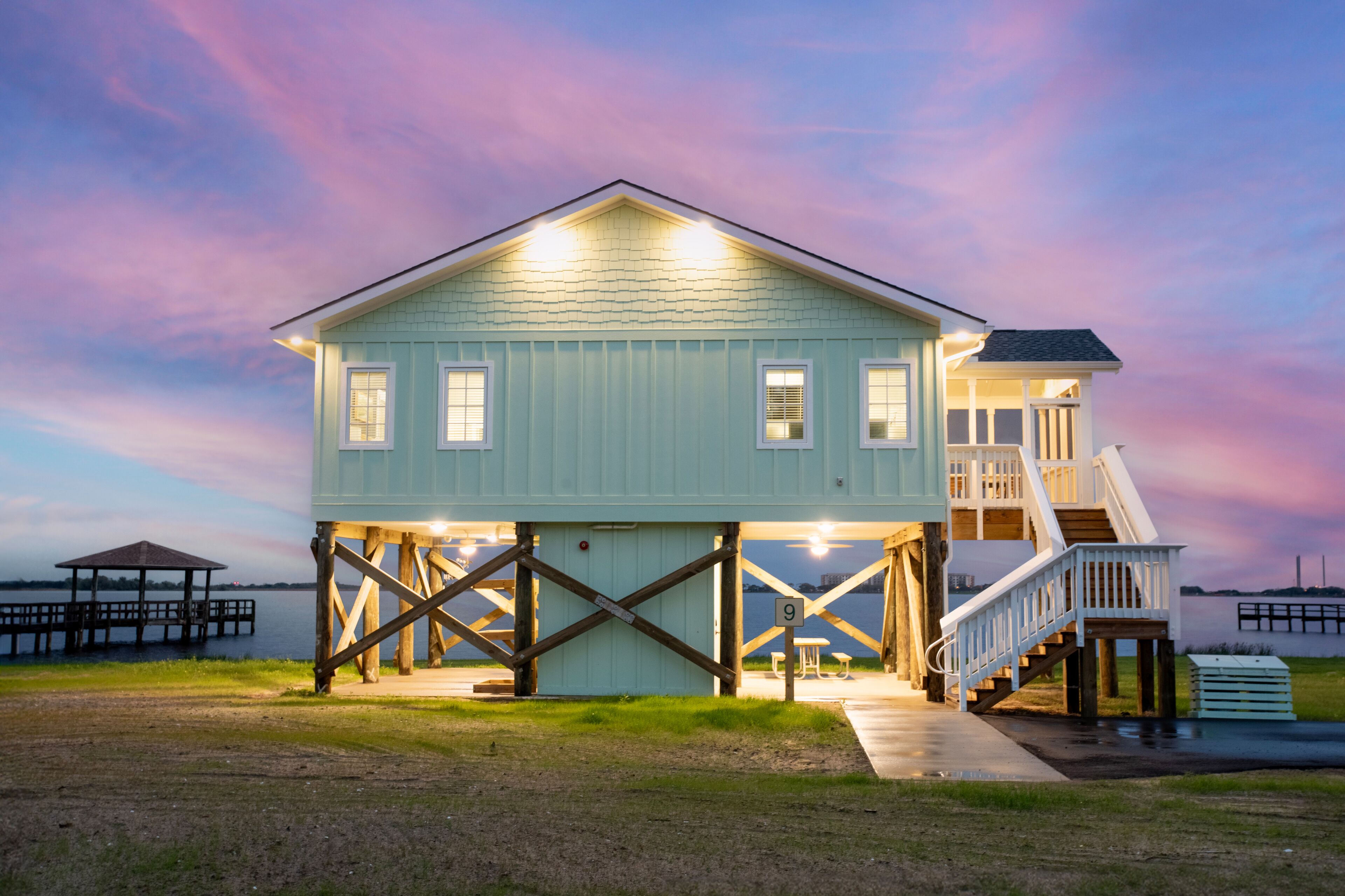 A waterfront house with a covered deck and a staircase leading to an upper level.