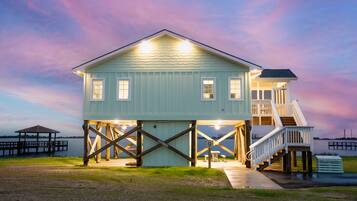 A waterfront house with a covered deck and a staircase leading to an upper level.