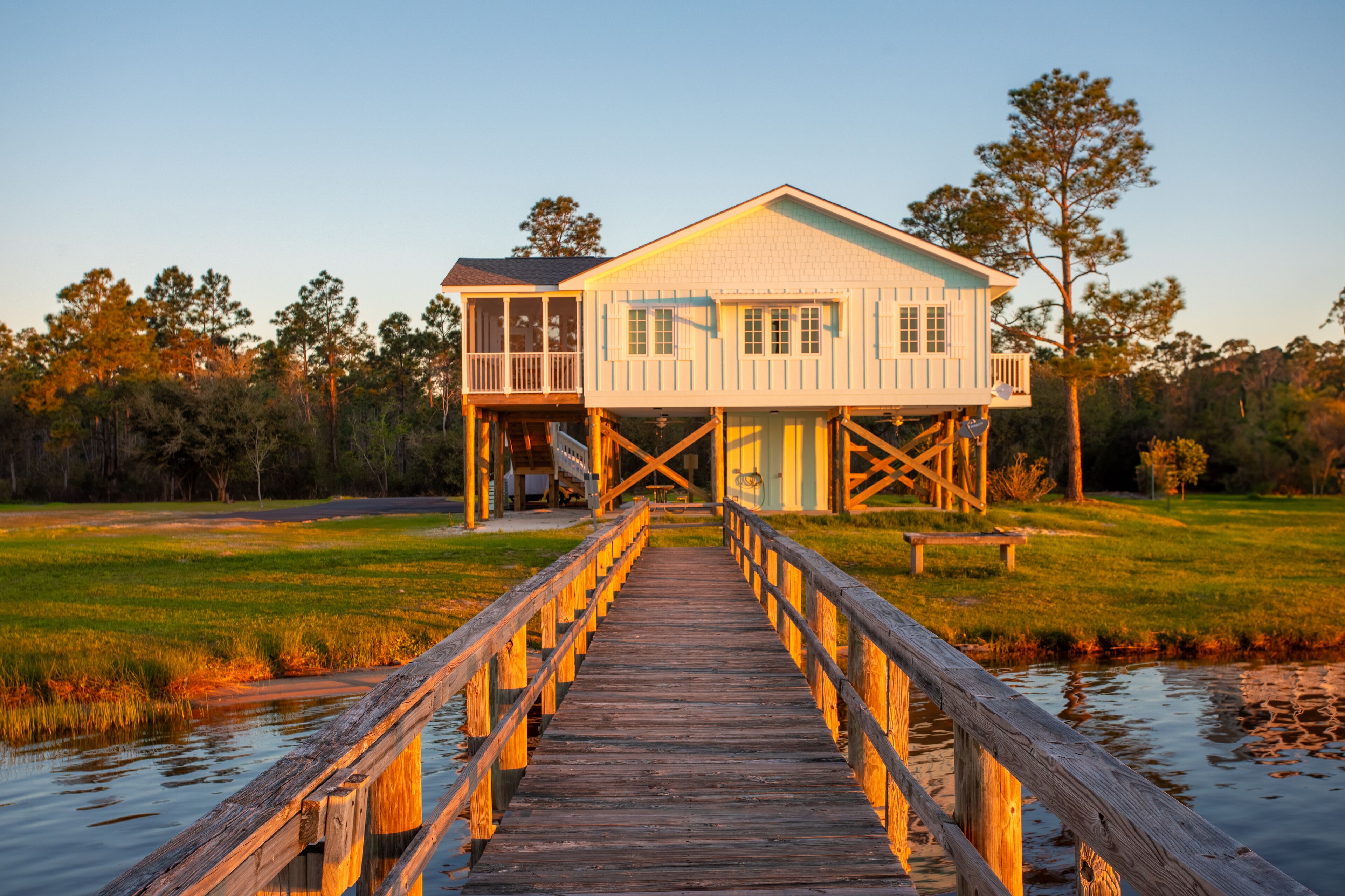 A wooden pier leading to a two-story house with a balcony, situated by a body of water.