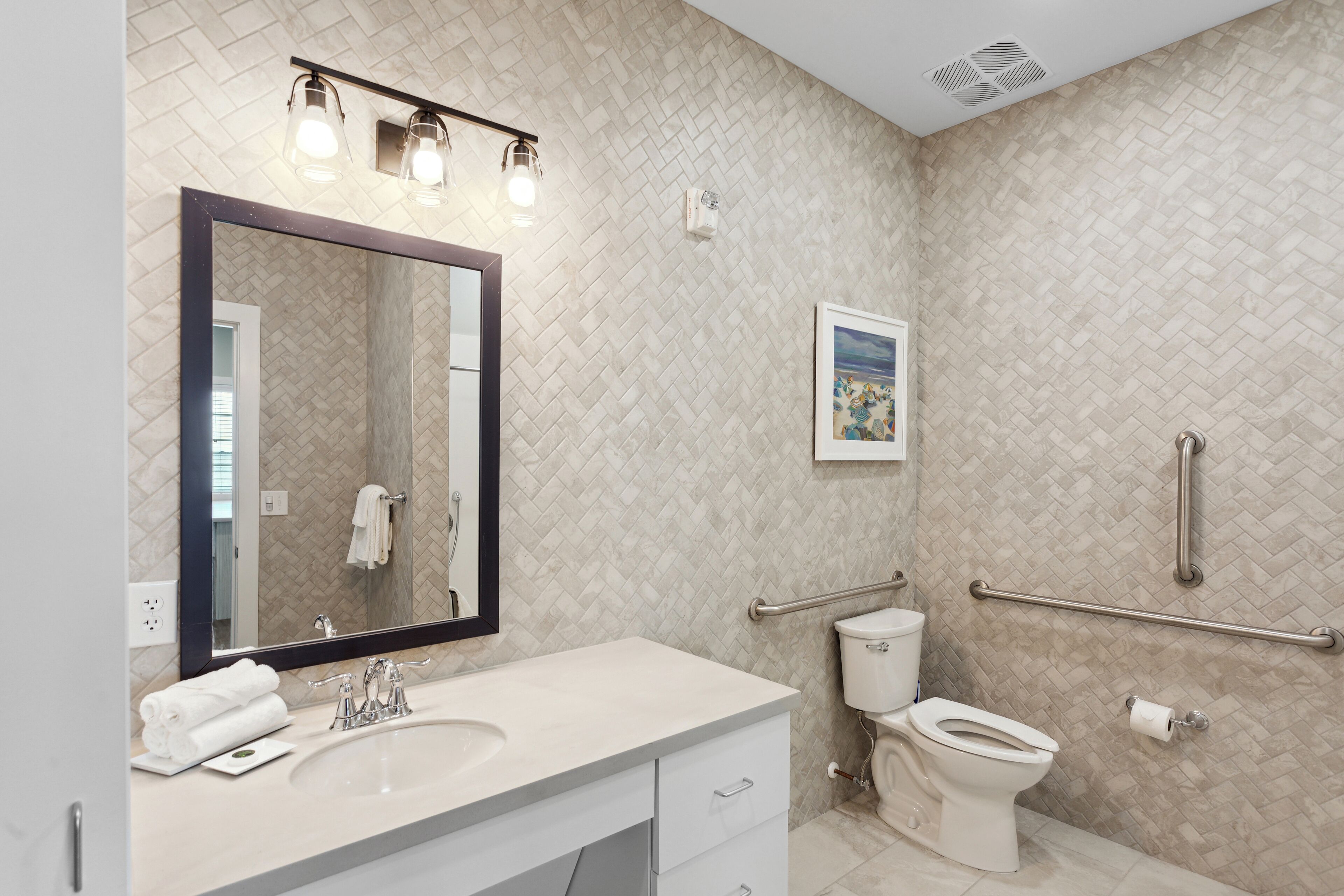 A modern bathroom with a large mirror, dual sinks, a toilet, and a handrail.