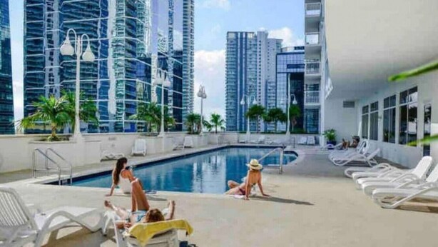 A rooftop pool area with lounge chairs, a swimming pool, and high-rise buildings in the background. - Splendid Unit with Parking in Brickell Miami (Miami)
