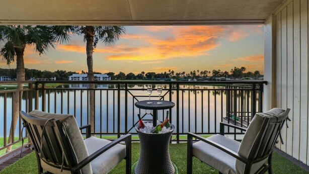 Un balcon avec deux chaises et une table, donnant sur un lac et offrant une vue sur le coucher du soleil.