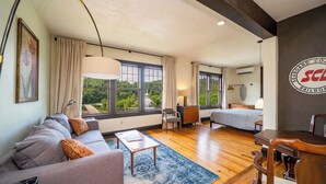 A modern hotel room with a large bed, a sofa, a desk, and a chair. There are large windows with curtains, a ceiling fan, and a logo on the wall. - Rent the Entire Historic Inn in Downtown Marshall (Marshall)