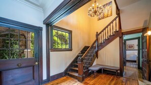 A wooden staircase with a bench at the bottom, a chandelier, and a door with a window. - Rent the Entire Historic Inn in Downtown Marshall (Marshall)