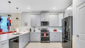 A modern kitchen with grey cabinets, stainless steel appliances, and a dishwasher. - NEW 9Bdrm Themed w Arcade near Disney & Universal (Kissimmee)