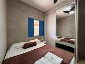 A bedroom with a bed, a nightstand, a mirror, and a window with blue shutters.