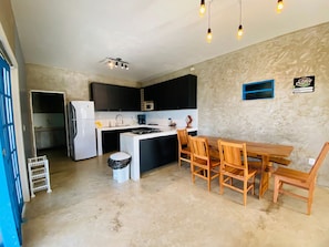 A compact kitchen with a refrigerator, microwave, and stove, a dining table with chairs, and a trash bin. - Casa Marataizes (Marataizes)