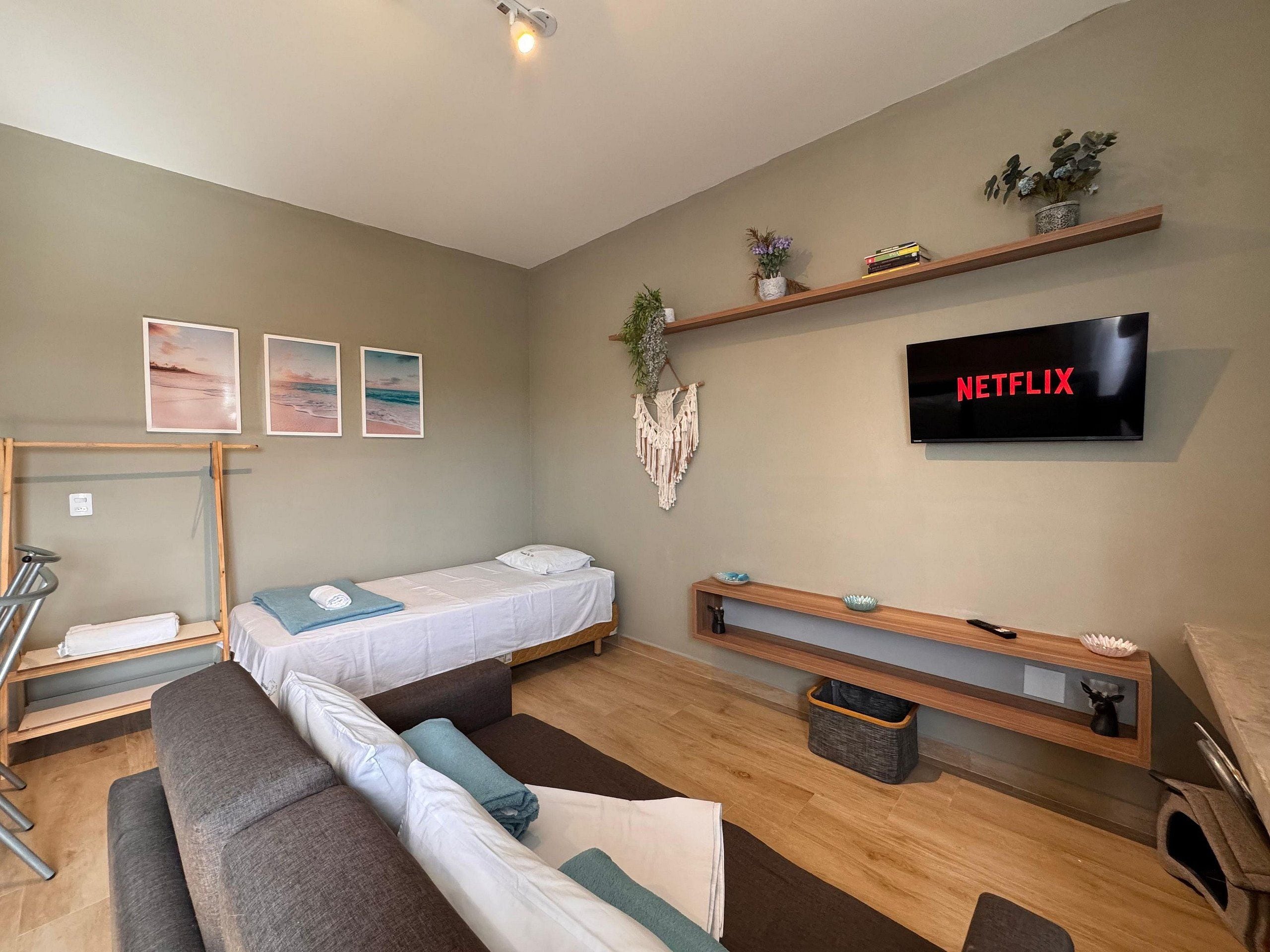 A modern living room with a sofa, a bed, a TV, and a wall-mounted shelf with plants.