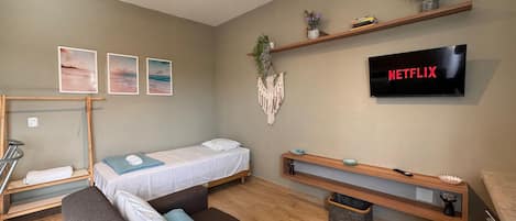 A modern living room with a sofa, a bed, a TV, and a wall-mounted shelf with plants.