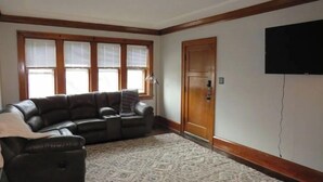 Un salon avec un canapé d’angle, un tapis à motifs et une porte en bois.