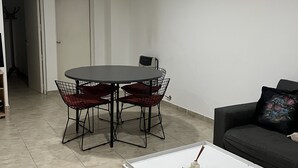 Ein Wohnzimmer mit einem runden Esstisch, roten Sitzsäcken, einem weißen Couchtisch und einem schwarzen Sofa mit einem Blumenkissen.