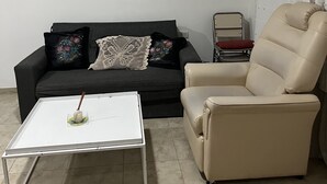 Ein Wohnzimmer mit einer schwarzen Couch, einem beigefarbenen Sessel, einem weißen Couchtisch und einem kleinen Beistelltisch.