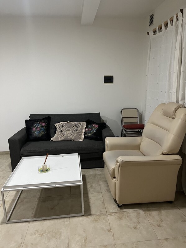 A living room with a black sofa, a beige armchair, a white coffee table, and a small side table.