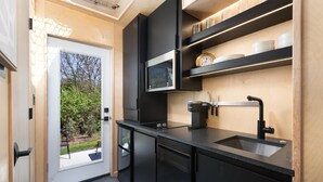 Una cocina compacta con armarios negros, microondas integrado, cafetera y lavabo.