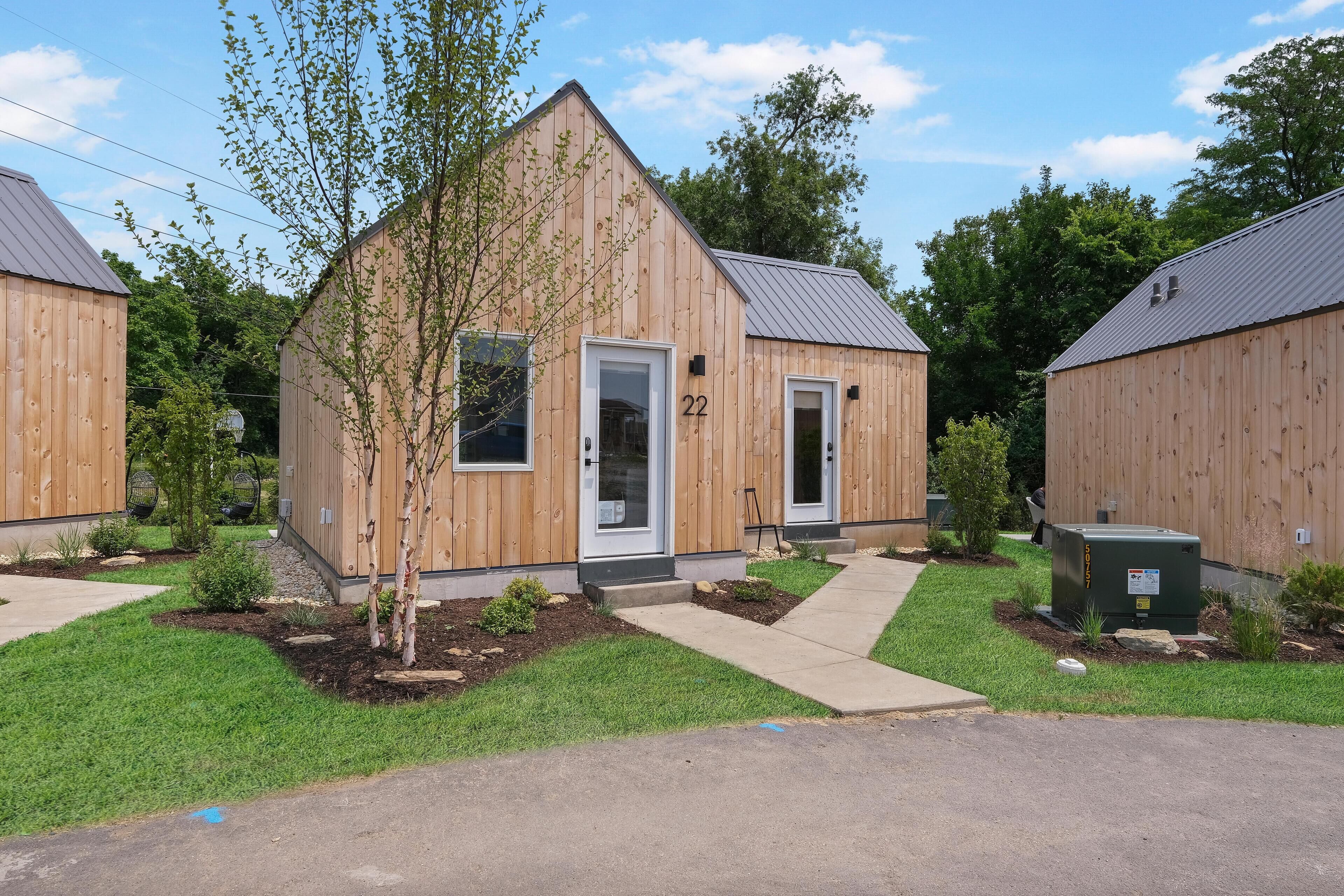 A small wooden building with a door labeled "22" and a small tree in front.