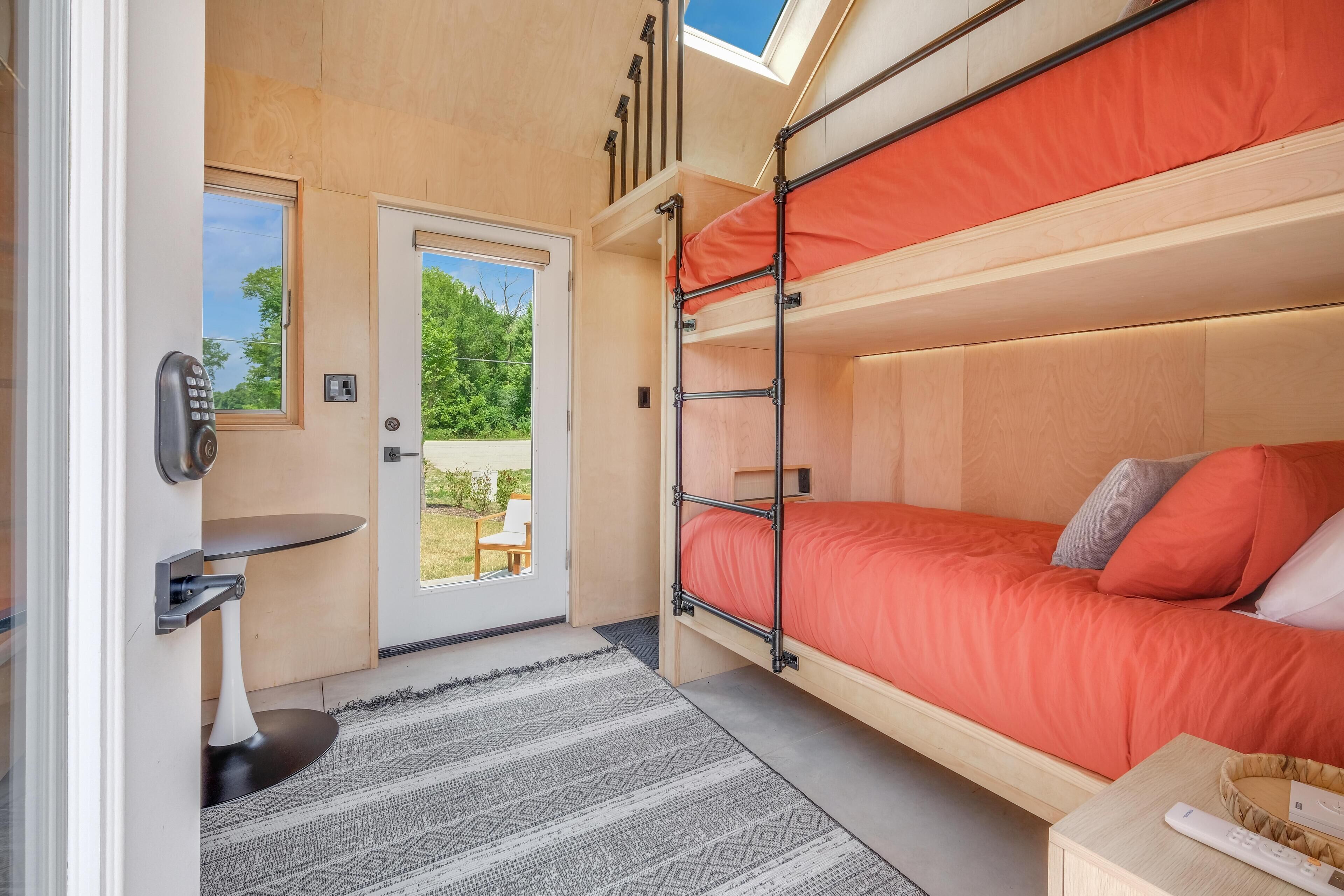 Une petite pièce comprenant un lit superposé, une petite table, une chaise et une porte donnant sur l’extérieur.