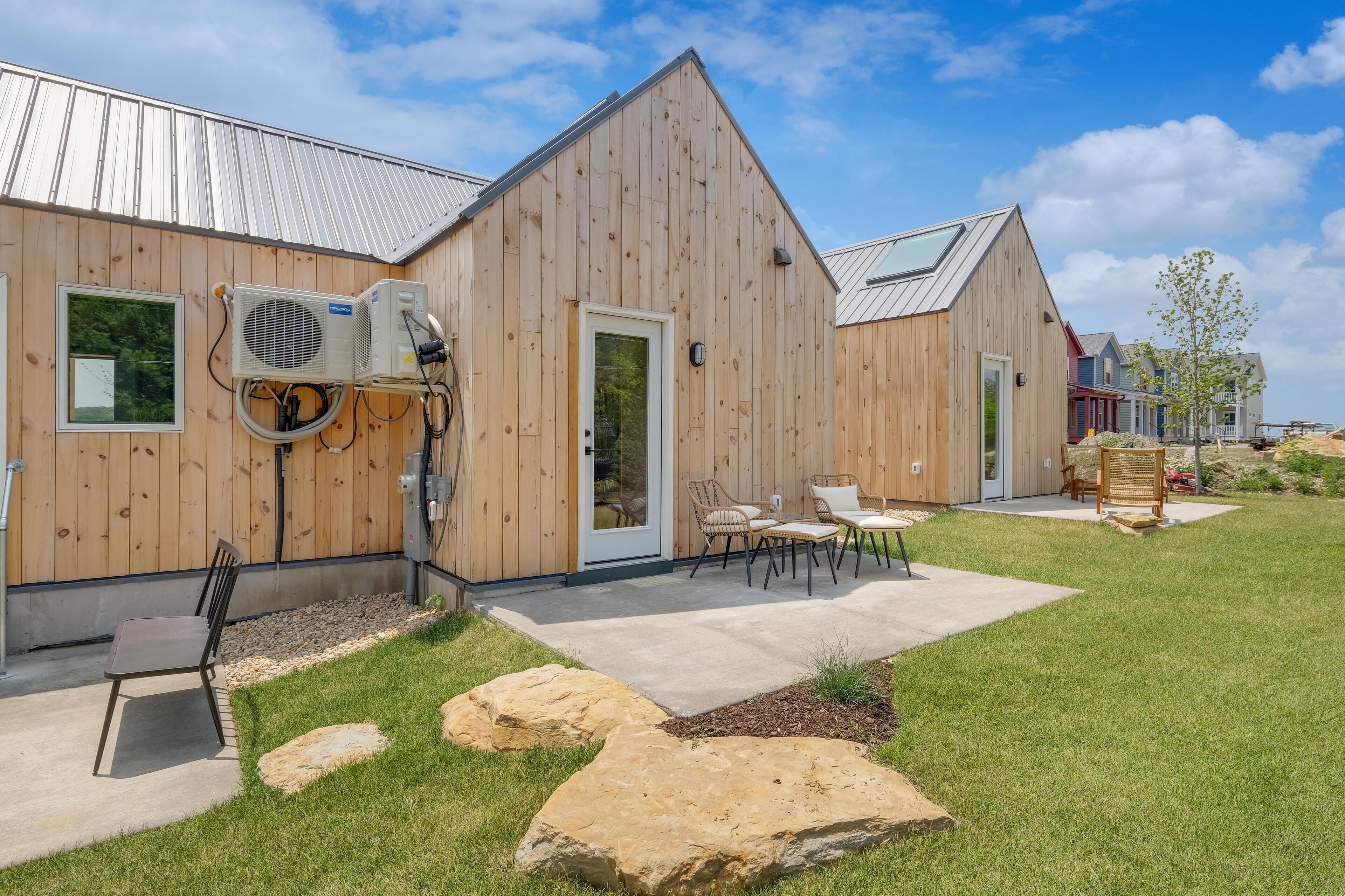 A wooden building with a metal roof, a covered patio with outdoor furniture, and a large air conditioning unit mounted on the exterior wall.