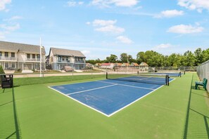 Een tennisbaan met een net, omgeven door een hek, en huizen op de achtergrond.