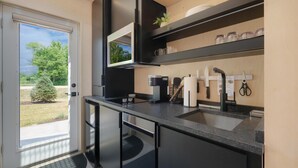 A modern kitchen with a large island, black cabinetry, and a view of the outdoors. - Bunkies-basecamp (Ottawa)