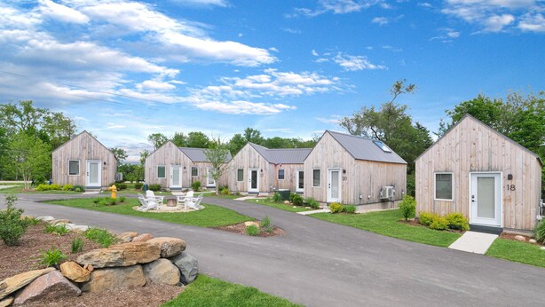A row of wooden cabins with numbered doors, a paved driveway, and a well-maintained lawn. - Bunkies-basecamp (Ottawa)