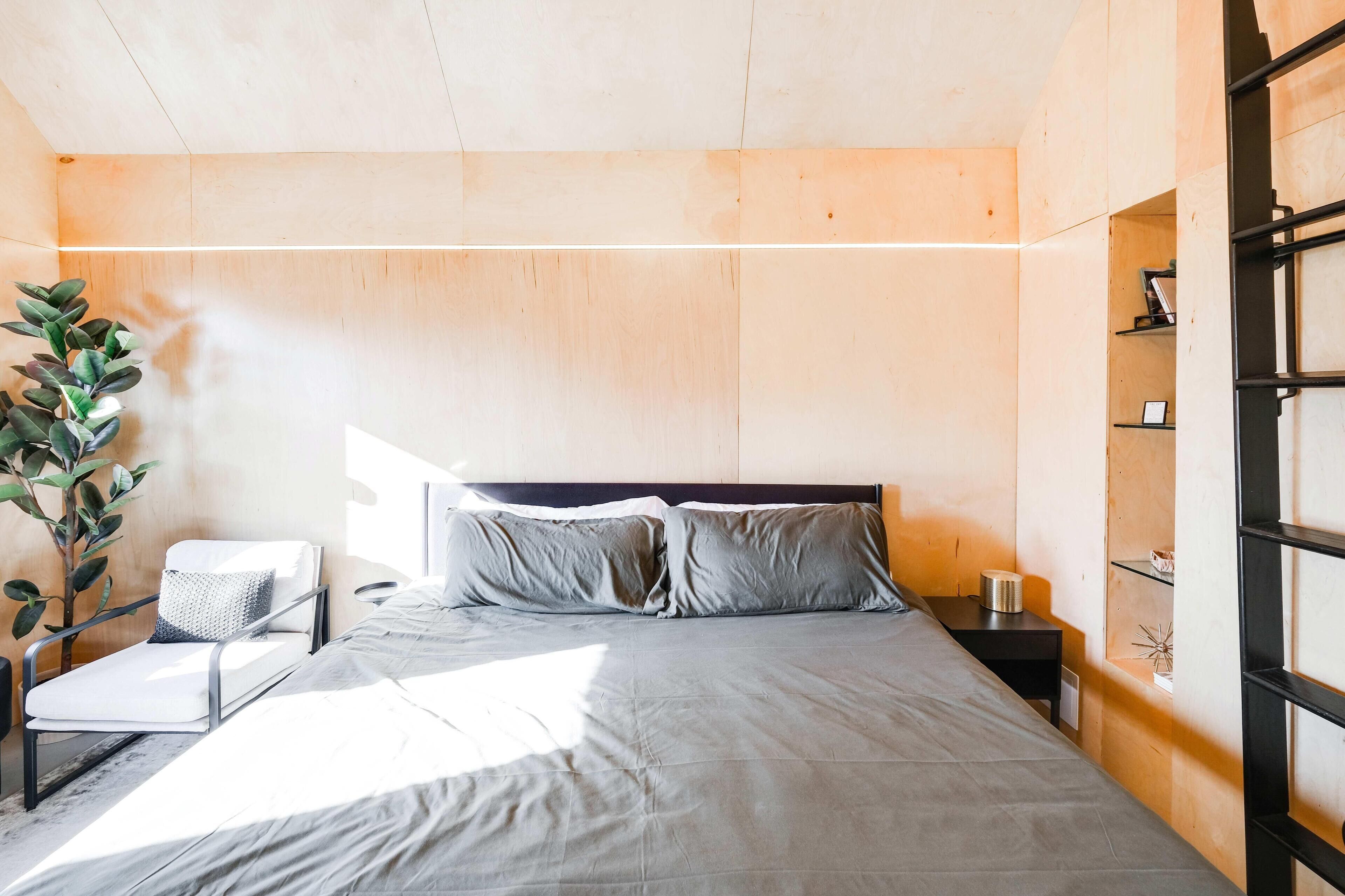 A modern bedroom with a large bed, a bedside table, a chair, and a potted plant.