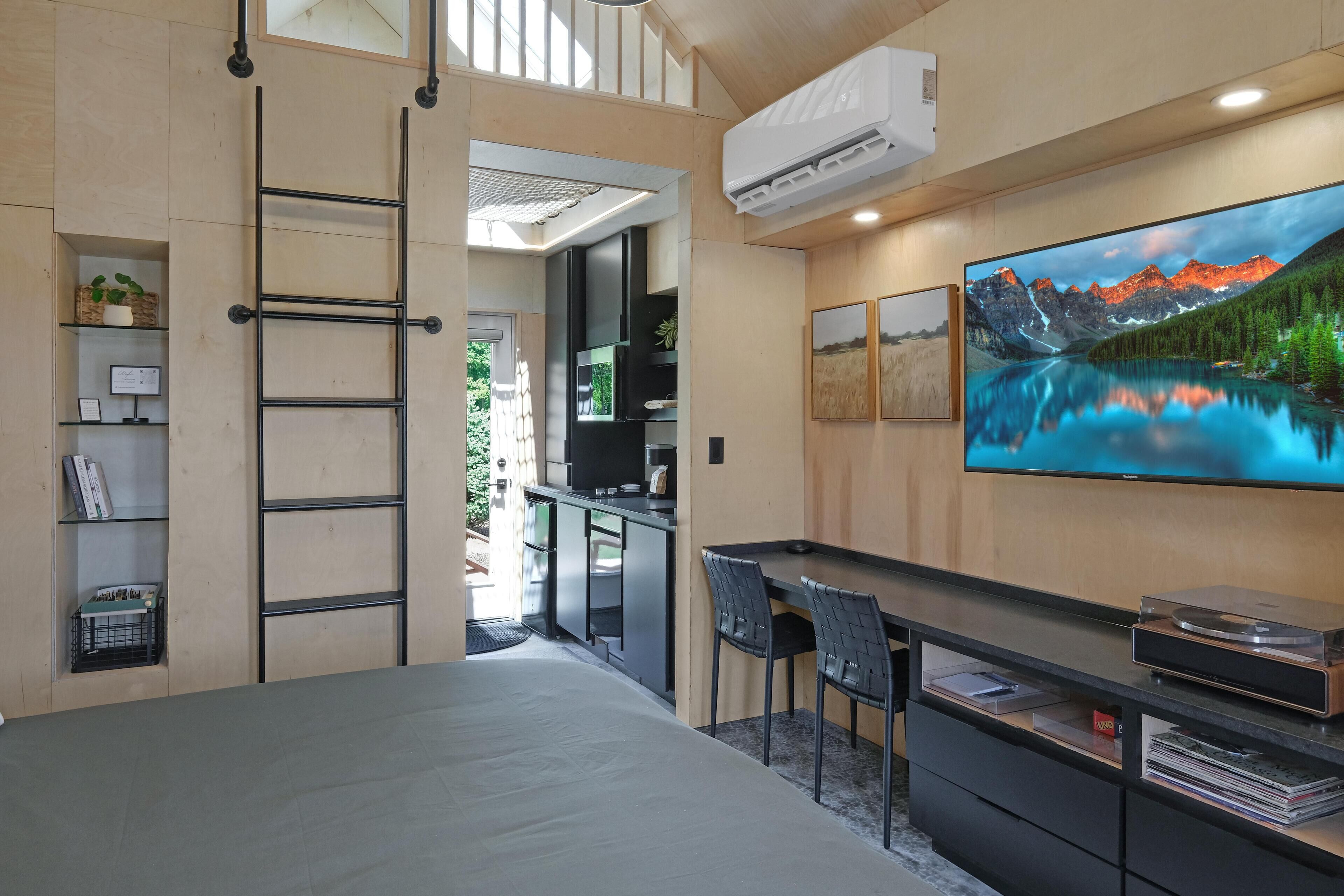 Una habitación de hotel moderna con una cama, un escritorio con sillas, un televisor y un ventanal con vistas a la montaña.