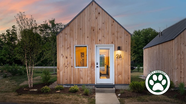 A wooden pet-friendly building with a door marked '26', a small window, and a pathway leading to the entrance. - Bunkies-the Commissioner (Ottawa)