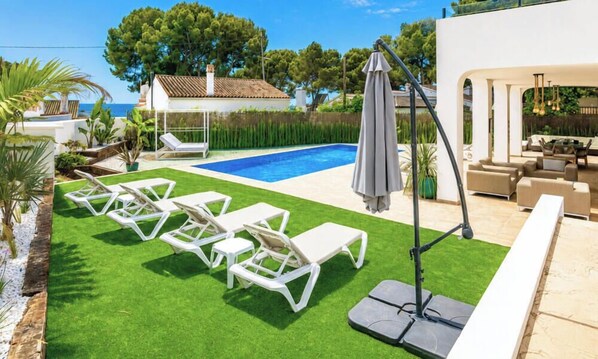 Une piscine avec des chaises longues, un espace salon couvert et une vue sur la mer.