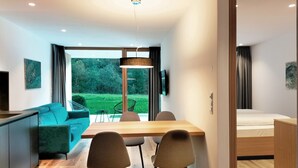 Un salon moderne avec un canapé, une table à manger et des chaises. Un téléviseur est fixé au mur et il y a une fenêtre avec des rideaux.