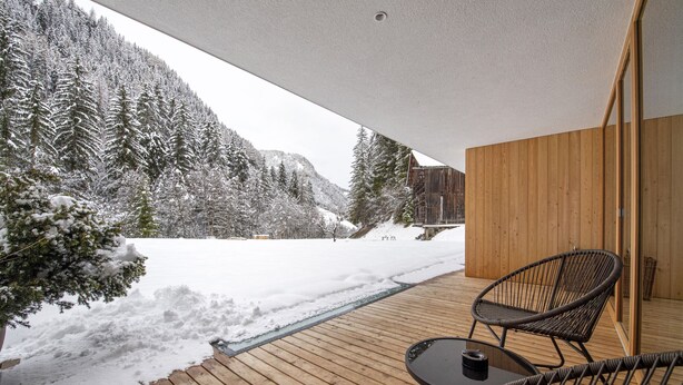 Eine Holzterrasse mit Blick auf eine verschneite Berglandschaft.