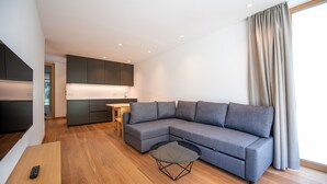 Ein modernes Wohnzimmer mit einem grauen Ecksofa, einem Glastisch und Holzboden.