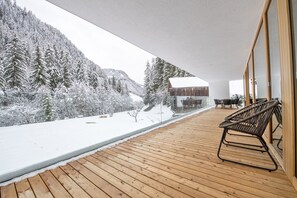 Una terraza de madera con vistas a árboles cubiertos de nieve y una cabaña.