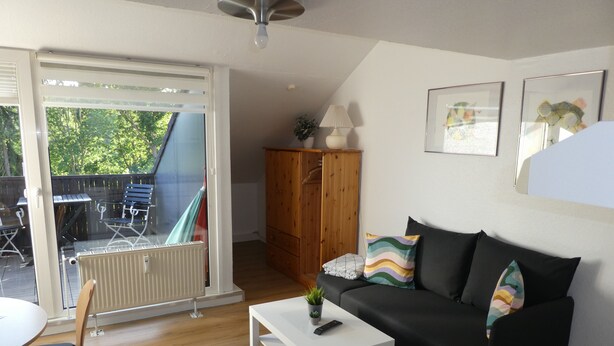 A living room with a black sofa, white coffee table, and a wooden cabinet. - Idyllic location on the Wennsee and 10 min walk to the beach with beautiful garden. (Scharbeutz)