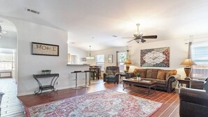 A spacious living room with a large rug, a sofa, and a coffee table. There is a dining area with chairs and a bar counter. - Texas Two Step - welcoming getaway at the steps of Sea World, near BMT! (San Antonio)