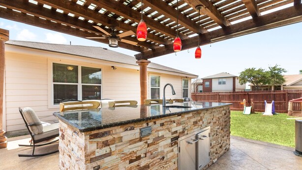 An outdoor kitchen with a stone countertop, a built-in sink, and a pergola overhead. - Texas Two Step - welcoming getaway at the steps of Sea World, near BMT! (San Antonio)