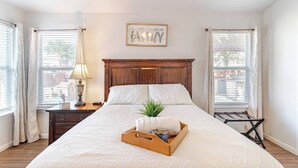 A neatly made bed with a wooden headboard, a bedside table with a lamp, and a tray with a plant and a towel. - Texas Two Step - welcoming getaway at the steps of Sea World, near BMT! (San Antonio)