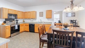 A modern kitchen with wooden cabinets, a stainless steel stove, and a dishwasher. There is a dining area with a wooden table and chairs. - Texas Two Step - welcoming getaway at the steps of Sea World, near BMT! (San Antonio)
