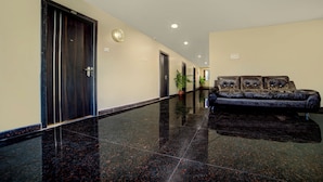 A hallway with a black leather sofa, a clock, and doors labeled with numbers. - Staro Hotel - Hotel In Vijayawada (Vijayawada)